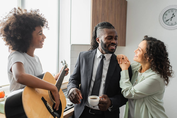 happy african american preteen girl playing acoustic guitar near cheerful parents  - Photo, Image