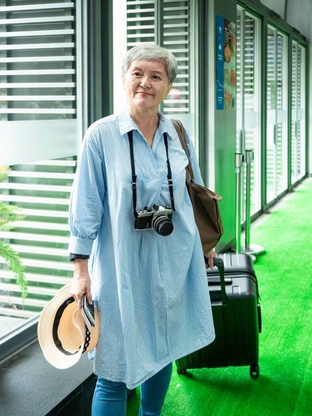 Portrait de femme asiatique âgée âgée des années 60 souriant debout avec valise sac à bagages et appareil photo pour le concept de voyage. - Photo, image