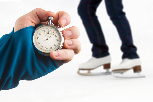 measuring speed on skates with a stopwatch. hand with a stopwatch on the background of the legs of a man skating on an ice rink - Photo, Image