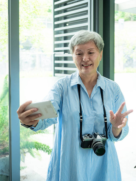 Portrait of happy senior adult elderly asia woman 60s taking selfie photo using smartphone camera for travel concept. - Zdjęcie, obraz