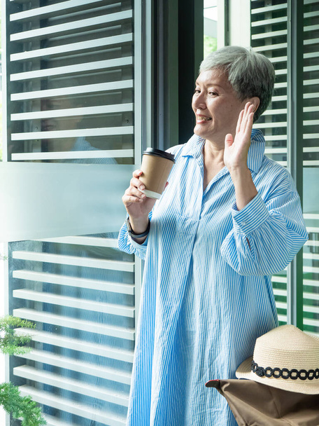 Πορτρέτο της ευτυχούς ηλικιωμένης γυναίκας της Ασίας 60 ετών κρατώντας χάρτινο κύπελλο, πίνοντας καφέ για ταξιδιωτικό concept. - Φωτογραφία, εικόνα