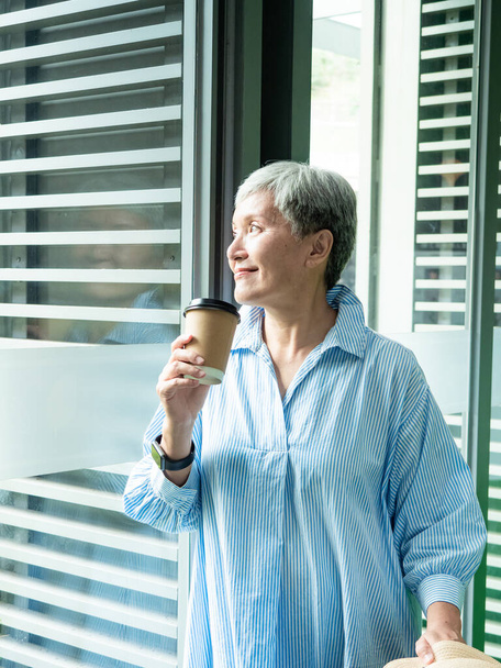 Portré boldog idősebb felnőtt idős ázsiai nő 60-as évek gazdaság papír pohár, ivás kávé utazási koncepció. - Fotó, kép