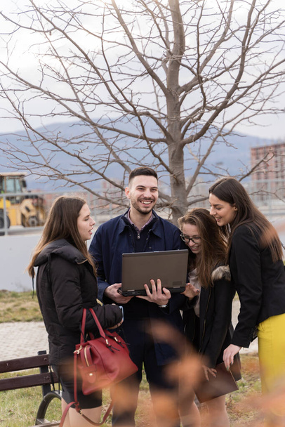 Group of young business people are smiling and looking at the lap top while standing outside - Photo, Image