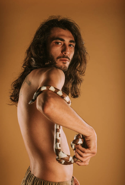 Όμορφος άντρας με το φίδι του βασιλιά της Καλιφόρνια που ποζάρει στο στούντιο. - Φωτογραφία, εικόνα