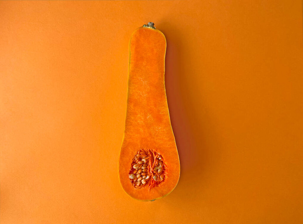 Half nutmeg pumpkin or gourd on orange background. Good for Halloween, Harvest or Thanksgiving commercials. Fall season vegetable backdrop. - 写真・画像