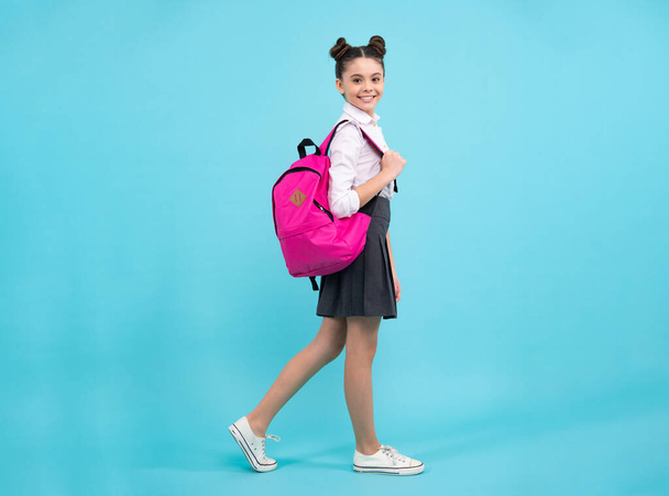 Iskoláslány egyenruhában, iskolatáskával. Tinédzser lány diák kék elszigetelt háttérrel. Tanulási tudás és gyermeknevelési koncepció. Boldog iskoláslány. - Fotó, kép
