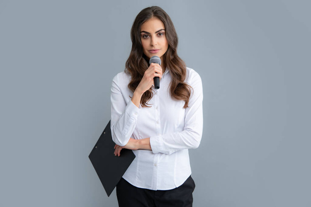 Young female journalist or businesswoman with microphone and clipboard on gray background - Foto, Imagen