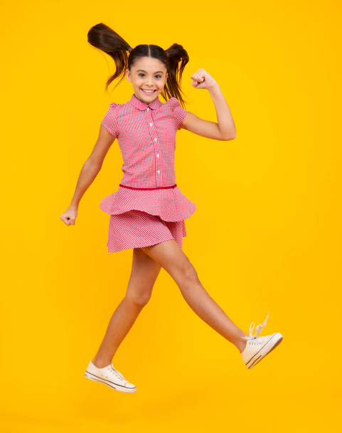 Boldog tinédzser, pozitív és mosolygó érzelmek tini lány. Teljes méretű fotó a pozitív tini lány ugrás mozgás nyári ruha, divat gyerekek ruha elszigetelt sárga háttér - Fotó, kép