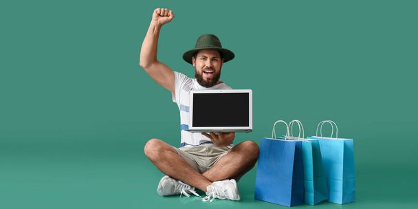 Yeşil arka planda dizüstü bilgisayarı ve alışveriş torbaları olan mutlu bir adam. Kara Cuma indirimi - Fotoğraf, Görsel