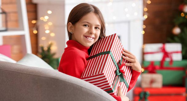 Мила усміхнена маленька дівчинка з різдвяним подарунком вдома
 - Фото, зображення