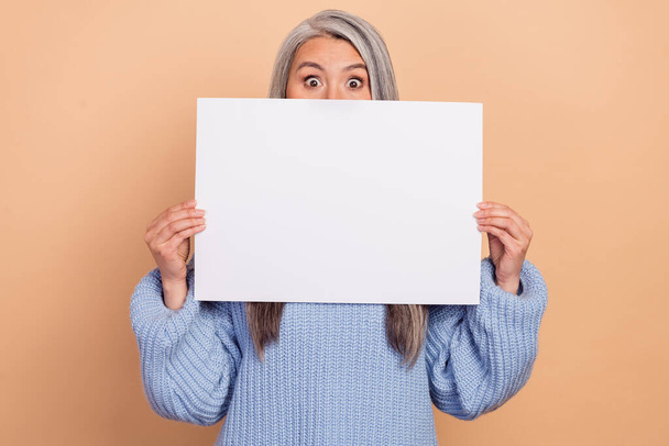 Photo of surprised funky lady pensioner dressed blue pullover poster empty space cover lips isolated beige color background. - 写真・画像