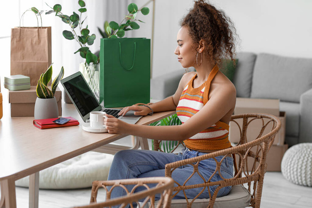 Jovem afro-americana com xícara de café e laptop compras on-line em casa - Foto, Imagem