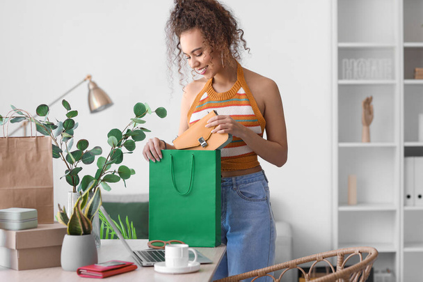 Young African-American woman taking new purchase from shopping bag at home - Foto, Bild