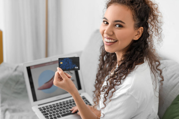 Giovane donna afro-americana con carta di credito e laptop shopping online a casa, primo piano - Foto, immagini