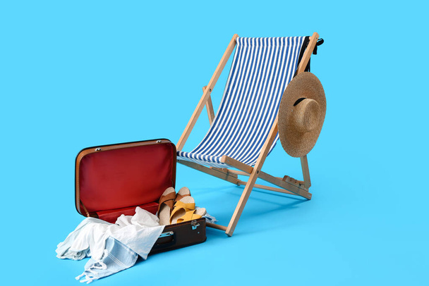 Καρέκλα καταστρώματος, βαλίτσα και αξεσουάρ παραλίας σε γαλάζιο φόντο - Φωτογραφία, εικόνα
