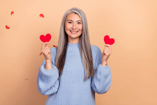 Photo of dreamy cute lady pensioner dressed blue pullover holding two small hearts isolated beige color background. - Valokuva, kuva
