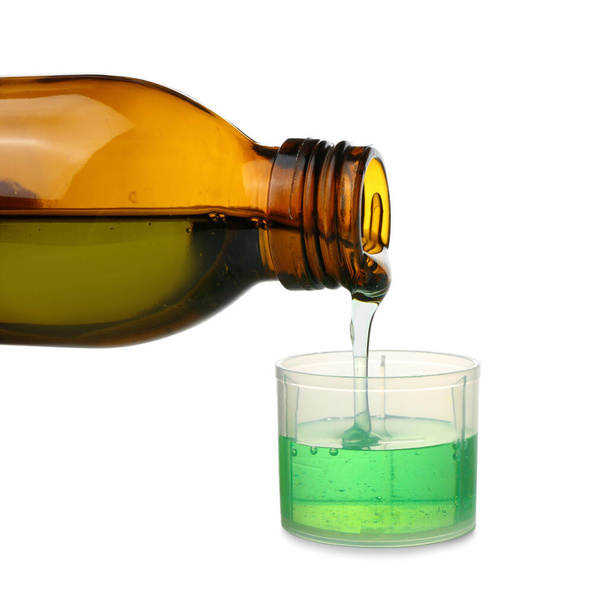 Verter el jarabe para la tos del frasco en una taza sobre fondo blanco - Foto, imagen