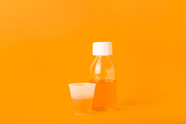 Бутылка сиропа от кашля и чашка на оранжевом фоне - Фото, изображение