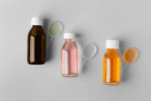 Flessen en lepels hoestsiroop op grijze ondergrond - Foto, afbeelding
