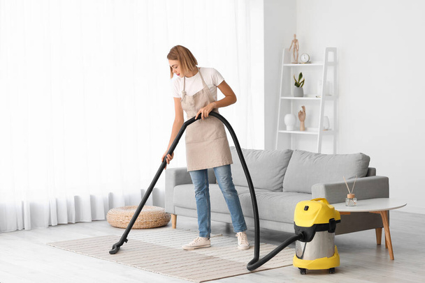 Jovem dona de casa tapete de limpeza com aspirador de pó em casa - Foto, Imagem