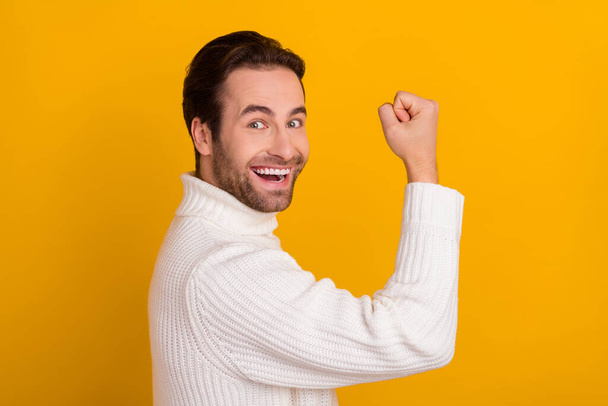 Photo of masculine virile guy raise fist rejoice lucky bet victory wear white sweater isolated yellow color background. - Photo, image