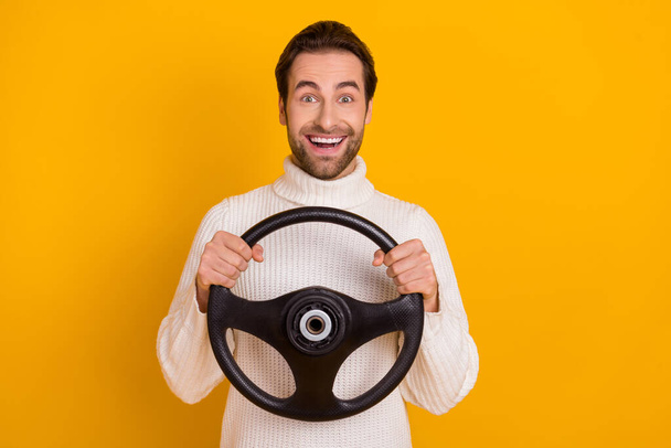 Photo of cute excited guy dressed white sweater holding steering wheel riding car isolated yellow color background. - Photo, Image