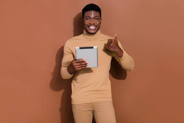 Portrait of attractive cheerful guy using device web site order showing thumbup isolated over brown color background. - Foto, imagen