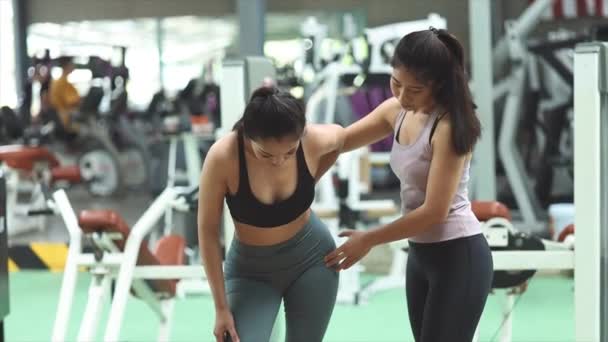 Zwei Frauen trainieren in einem Fitnesscenter, weibliche Trainerin trainiert Klienten bei Übungen, wärmt sich vor dem Sport auf und geht ins Fitnesscenter zur Gesundheitsvorsorge. Fitness-Trainingskonzept. - Filmmaterial, Video