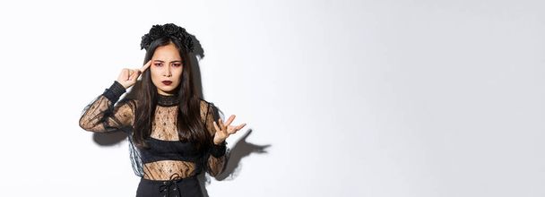 Frustrated asian woman in halloween costume arguing and complaining, scolding for something stupid, pointing finger at head and grimacing, standing over white background. - Foto, Imagen