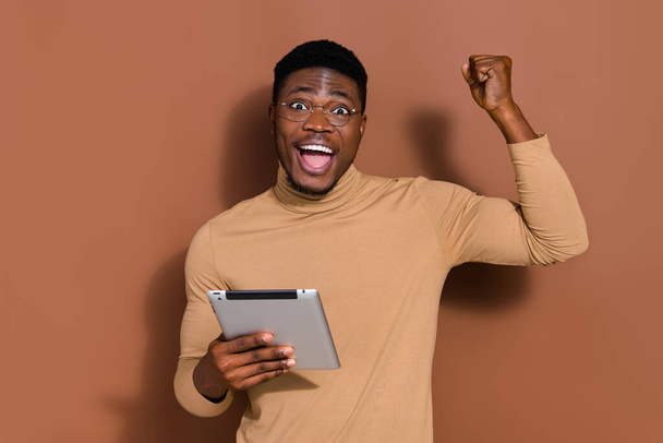 Portrait of attractive cheerful lucky guy using device web site order rejoicing having fun isolated over brown color background. - Photo, Image
