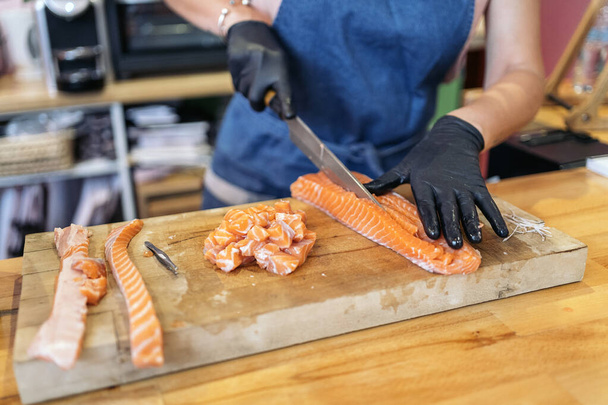 Unrecognized restaurant worker wearing latex gloves using a knife to cut salmon. - Photo, Image