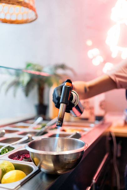Unrecognized restaurant worker preparing poke bowl and using kitchen blowtorch. - Foto, Bild
