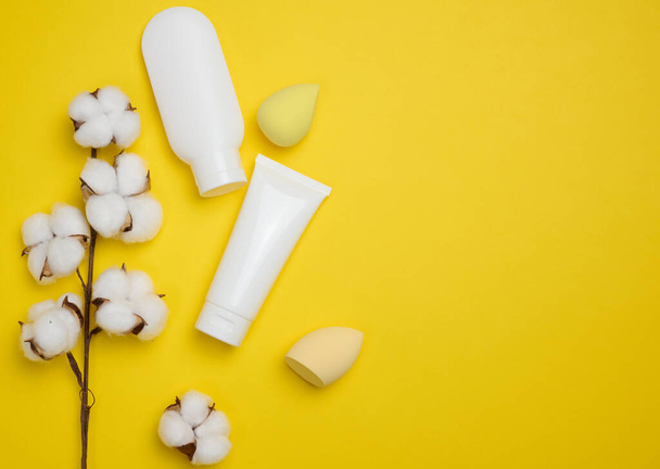 Tubos de plástico blanco y frasco para crema, gel y otros cosméticos y esponjas sobre un fondo amarillo, vista superior - Foto, Imagen