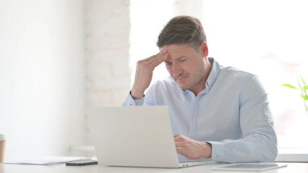 Hombre de mediana edad que tiene dolor de cabeza mientras trabaja en el ordenador portátil - Foto, imagen