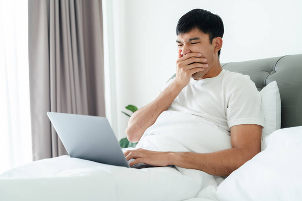 Hombre soñoliento bostezando en la cama usando computadora portátil. - Foto, imagen