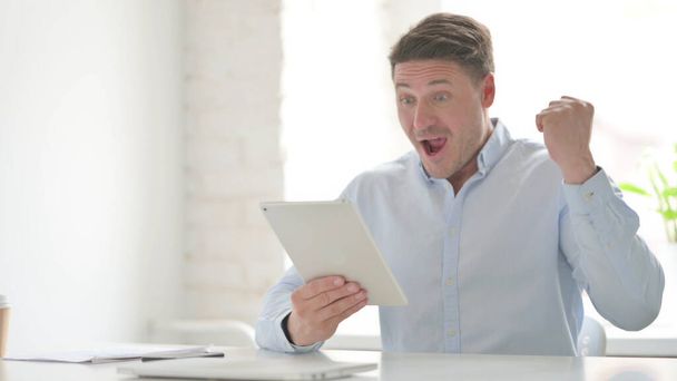 Uomo di mezza età che celebra il successo sul tablet in ufficio - Foto, immagini