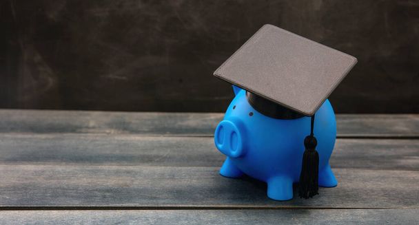 Plan financiero de educación, beca, préstamo estudiantil y costo escolar. Piggybank azul con gorra de graduación en madera. - Foto, Imagen
