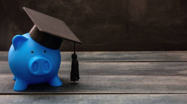 Plan financiero de educación, beca, préstamo estudiantil y costo escolar. Piggybank azul con gorra de graduación en madera. - Foto, imagen