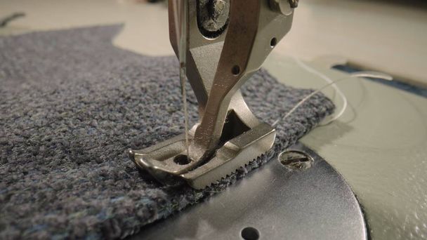 Presser foot of the sewing machine presses gray woolen fabric. A steel sharp needle with a thread is raised up. Macro shot of sewing gray woolen fabric with sewing machine. Industrial sewing equipment - 写真・画像