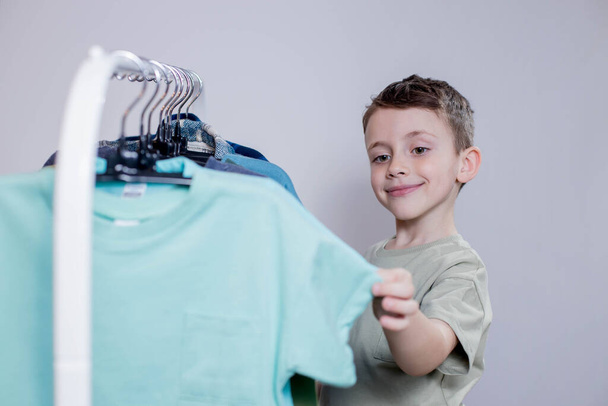 Boy preschooler standing by the hangers, racks up clothes, and chooses clothes for today. - Foto, Imagen