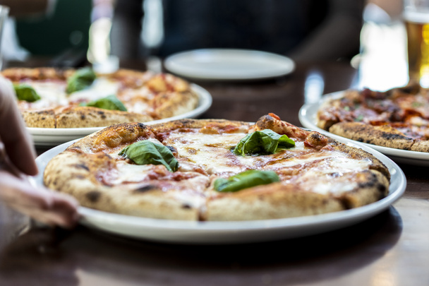 Vista de cerca de una pizza estilo napolitano Margherita con mozzarella de búfalo, salsa de tomate y albahaca - Mano de camarero que sirve pizza en el restaurante de pizza - Foto, imagen