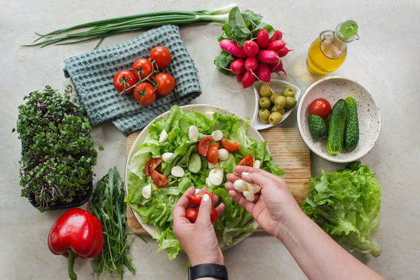Υγιεινή διατροφή και προετοιμασία σαλάτας λαχανικών με μαρούλι, ντομάτα και μοτσαρέλα. Κάτοψη της χορτοφαγικής ποικιλίας σε λευκό ρουστίκ ξύλινο τραπέζι - Φωτογραφία, εικόνα