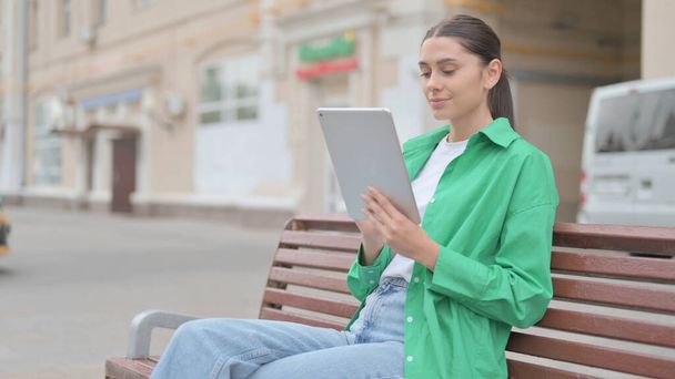 Young Woman using Tablet while Sitting Outdoor on Bench - Foto, Imagen