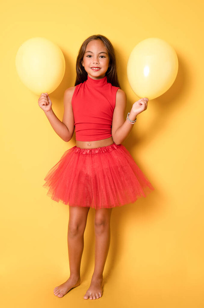 Lovely little girl wearing red clothes playing with yellow balloons. Happy girl face, positive and smiling emotions. Party celebration concept. - Foto, Imagen