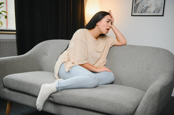 girl holding her head, woman has a headache. sad female sitting on couch. - Foto, immagini