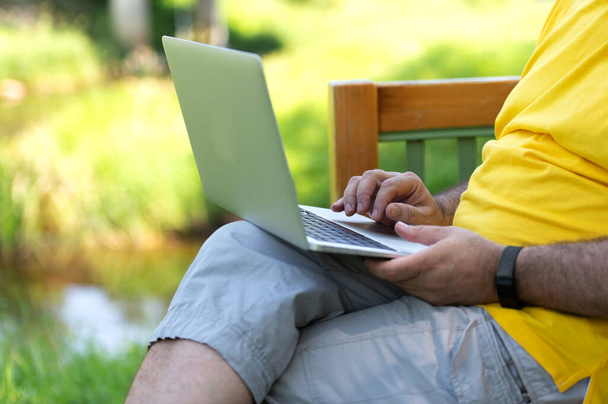 公園に座っている間にノートパソコンのキーボードを操作して入力する男 - 写真・画像