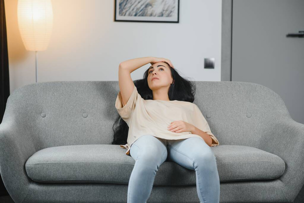 Beautiful hispanic woman in painful expression holding her belly suffering menstrual period pain lying sad on home bed having tummy cramp in female health concept. - Photo, Image