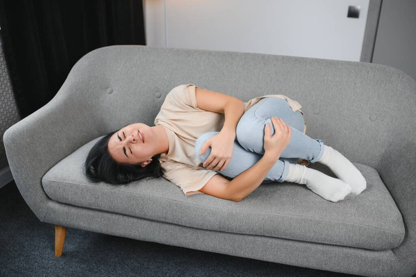 Young woman suffering from abdominal pain at home. Gynecology concept. - 写真・画像