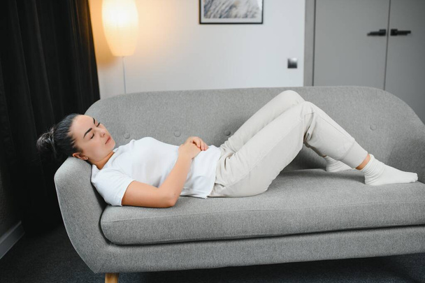 Young woman suffering from menstrual cramps at home. Gynecology. - 写真・画像