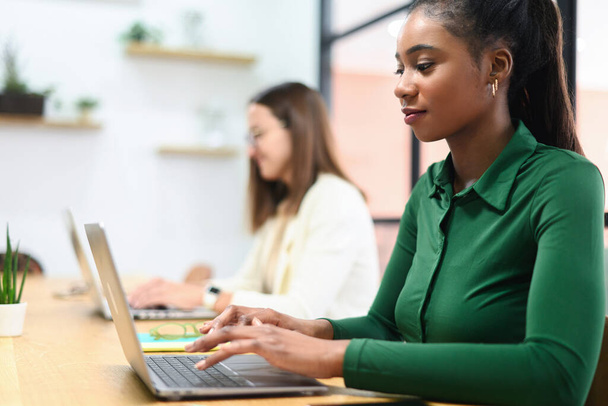 Side view of concentrated african-american female employee using laptop computer, smiling black businesswoman responds emails, freelancer woman working sitting in coworking space - Fotoğraf, Görsel